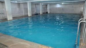 Une piscine intérieure à l’eau claire, avec des murs carrelés et des échelles en métal.