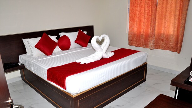 Une chambre d’hôtel avec un lit, des oreillers rouges, une couverture rouge et une décoration en forme de cœur faite avec une serviette.