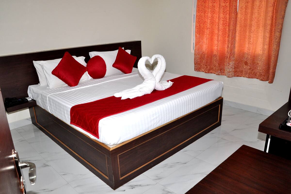A hotel room with a bed, red pillows, a red blanket, and a heart-shaped towel decoration.