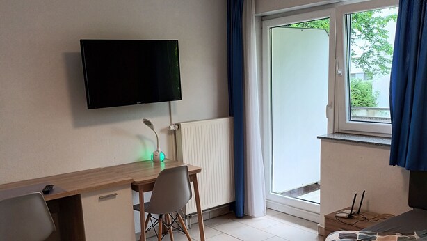 Een slaapkamer met een bed, een bureau met stoel, een televisietoestel en een raam met gordijnen.