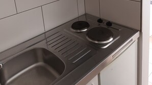 Een keuken met witte kasten, een roestvrijstalen spoelbak en een tweepits elektrische kookplaat.