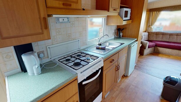 Une cuisine compacte équipée d’une cuisinière à gaz, d’un évier et d’un four à micro-ondes, de placards en bois et d’une fenêtre avec des rideaux.
