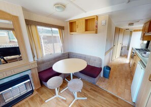 Ett kompakt inre utrymme i husbilen med ett litet kök, en sittgrupp med bord och stolar samt en tv.
