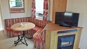 Une pièce confortable avec un canapé, une petite table, un téléviseur et une fenêtre avec des rideaux.