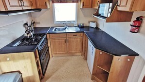 Une cuisine de taille réduite, dotée de meubles en bois, d’une cuisinière, d’un évier et d’un four à micro-ondes.