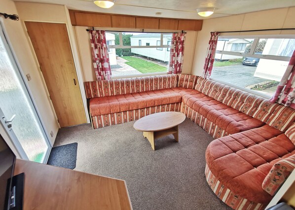 L’intérieur d’une caravane est aménagé avec un canapé incurvé, une petite table ronde et une porte donnant sur l’extérieur.