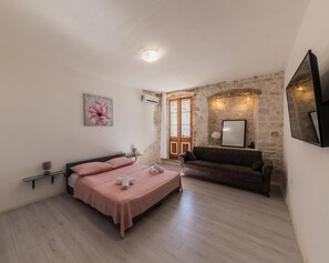 A bedroom with a bed, a sofa, a stone wall, and a door leading to a balcony. - A 1 - Spacious apt on the Seafront With Terrace (Kastela)
