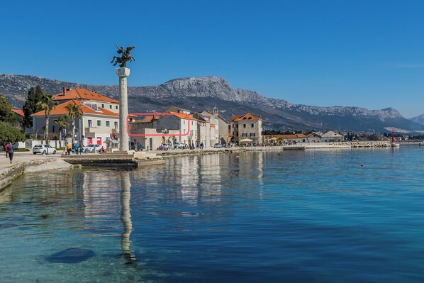 A waterfront promenade with buildings, a statue, and mountains in the background. - A 1 - Spacious apt on the Seafront With Terrace (Kastela)