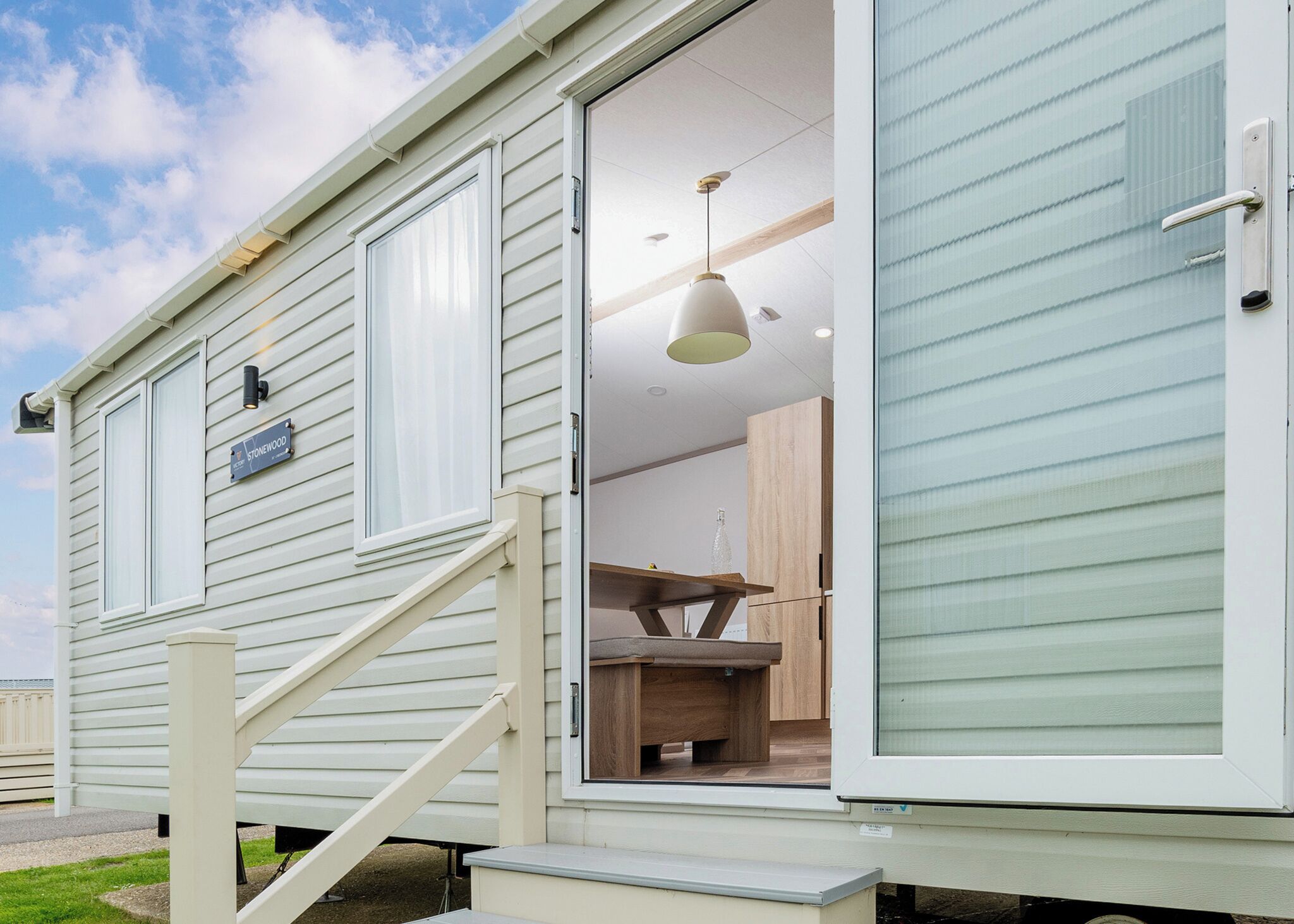 A mobile home with a staircase leading to the entrance, a dining area with a table and chairs, and a sign indicating the name 'Stonewood.'