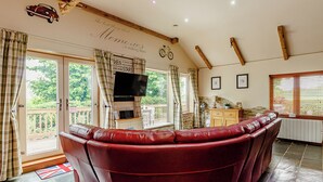 A living room with a red leather sofa, a television, and a balcony with curtains. - 1 bedroom accommodation in Haswell, Nr Durham (Haswell, Nr Durham)