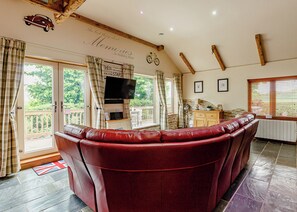 A living room with a red leather sofa, a television, and a balcony with curtains. - 3 bedroom accommodation in Haswell, Nr Durham (Haswell, Nr Durham)