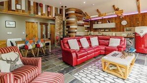 A modern living room with a red leather sofa, striped armchairs, a wooden coffee table, and a kitchen area with a red appliance. - 1 bedroom accommodation in Haswell, Nr Durham (Haswell, Nr Durham)