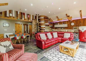 A modern living room with a red leather sofa, striped armchairs, a wooden coffee table, and a kitchen area with a red appliance.