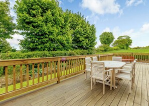A wooden deck with a table and chairs, surrounded by a wooden railing and lush greenery.