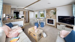 A compact living space with a kitchenette, a seating area, a television, and a fireplace. - Spacious and modern 12ft-wide caravan with one double and two twin. (New Quay)