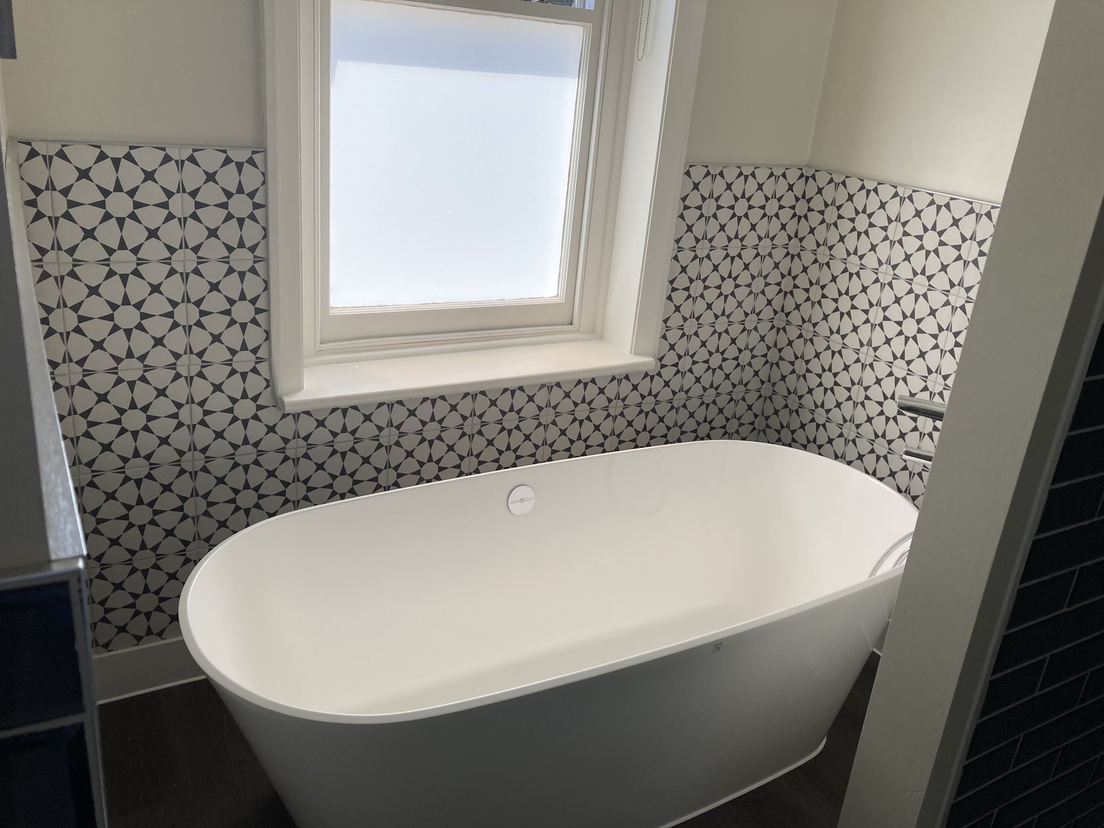 Een moderne badkamer met een vrijstaand bad, tegels met een geometrisch patroon en een raam boven het bad.