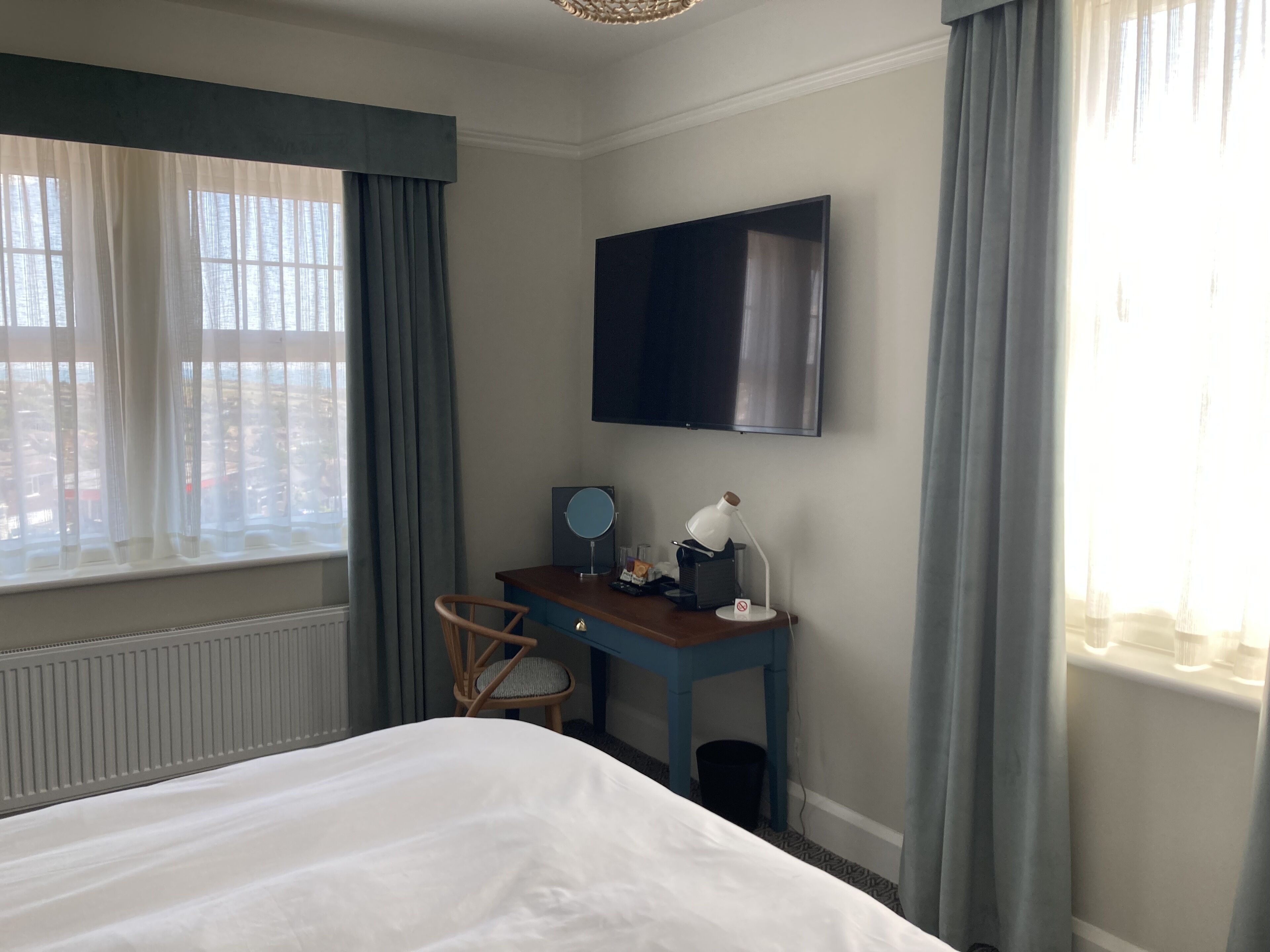A hotel room with a bed, a desk with a chair, a TV, and a window with curtains.