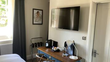 A hotel room with a bed, a desk with a chair, a television, a window with curtains, a framed picture on the wall, and a sign with "Guest Information".