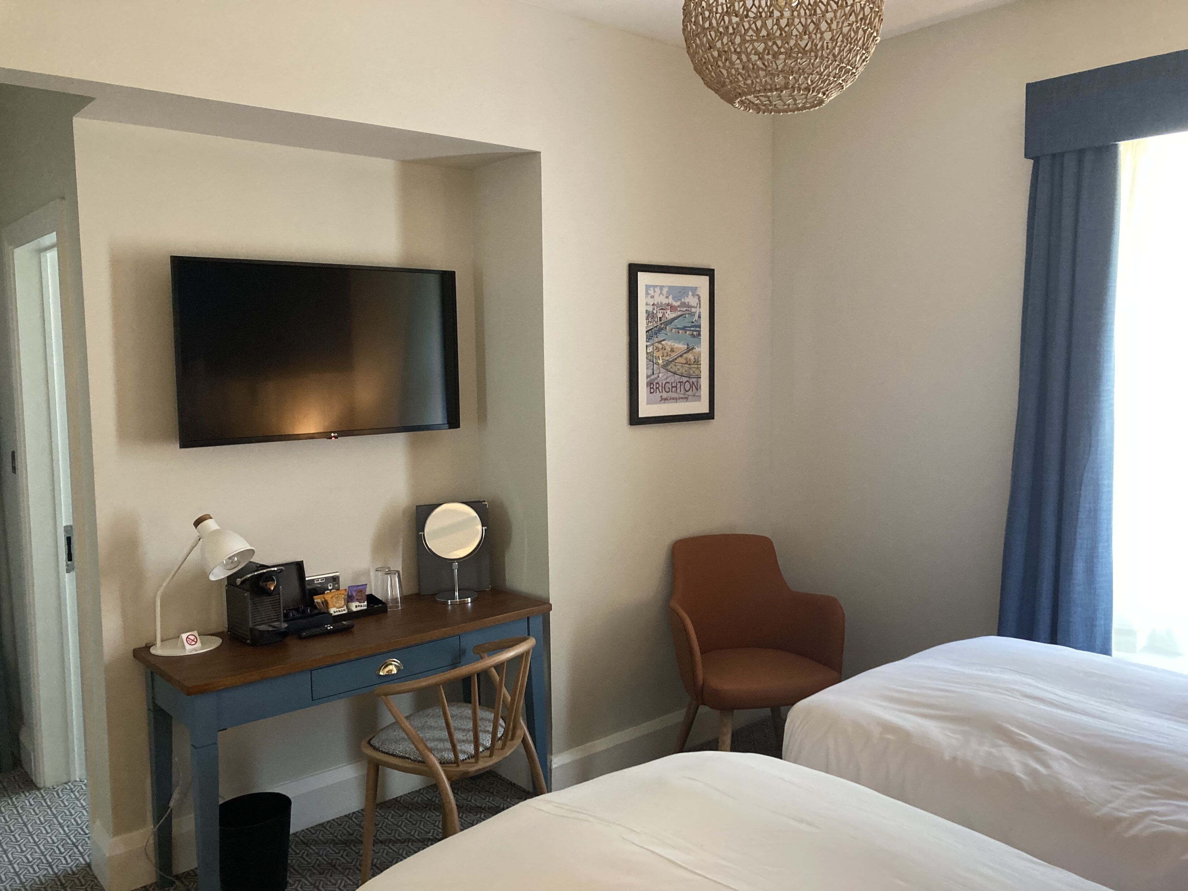 A hotel room with a bed, a desk with a chair, a television, a framed picture, and a window with curtains.