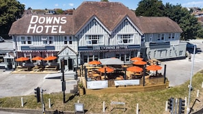 Un hôtel de deux étages, avec une enseigne indiquant « The Downs Hotel » et « Chambres, bar et restaurant ». Il y a des espaces de détente en plein air avec des parasols orange.