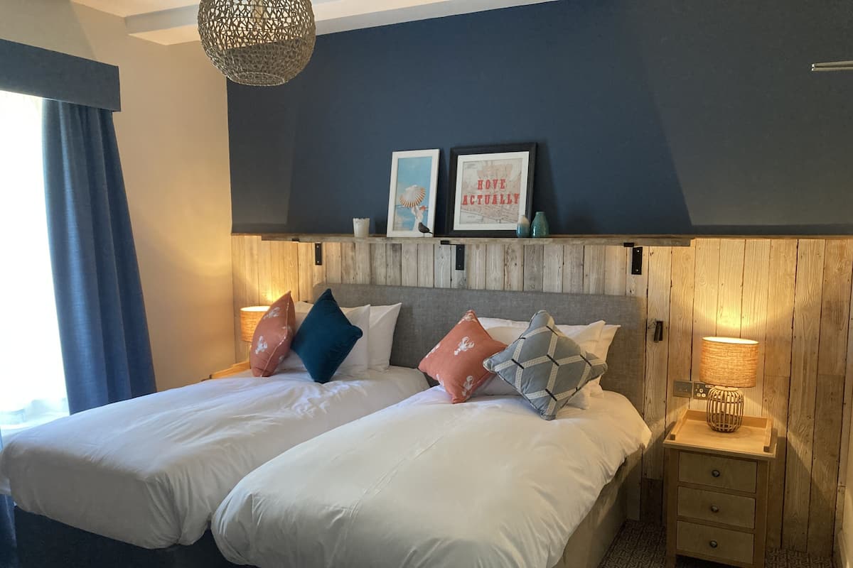 A double bed with white linens, two bedside tables with lamps, a wooden headboard, and a wall-mounted shelf with decorative items.