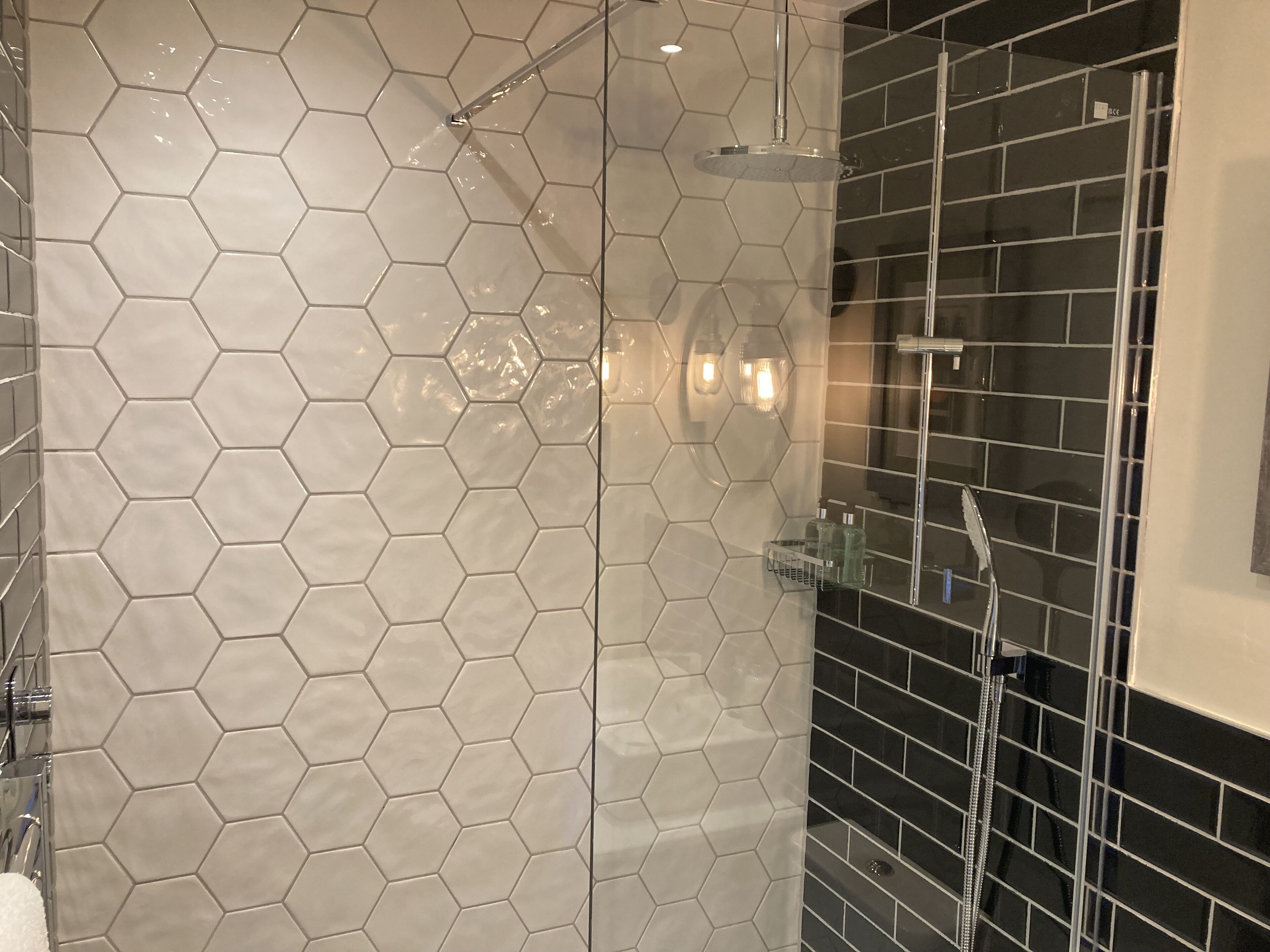 A bathroom with hexagonal tile walls, a shower area with black tiles, and a glass shower enclosure.