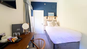 Habitación de hotel con cama, escritorio con computadora y teléfono, espejo y puerta que da al baño.