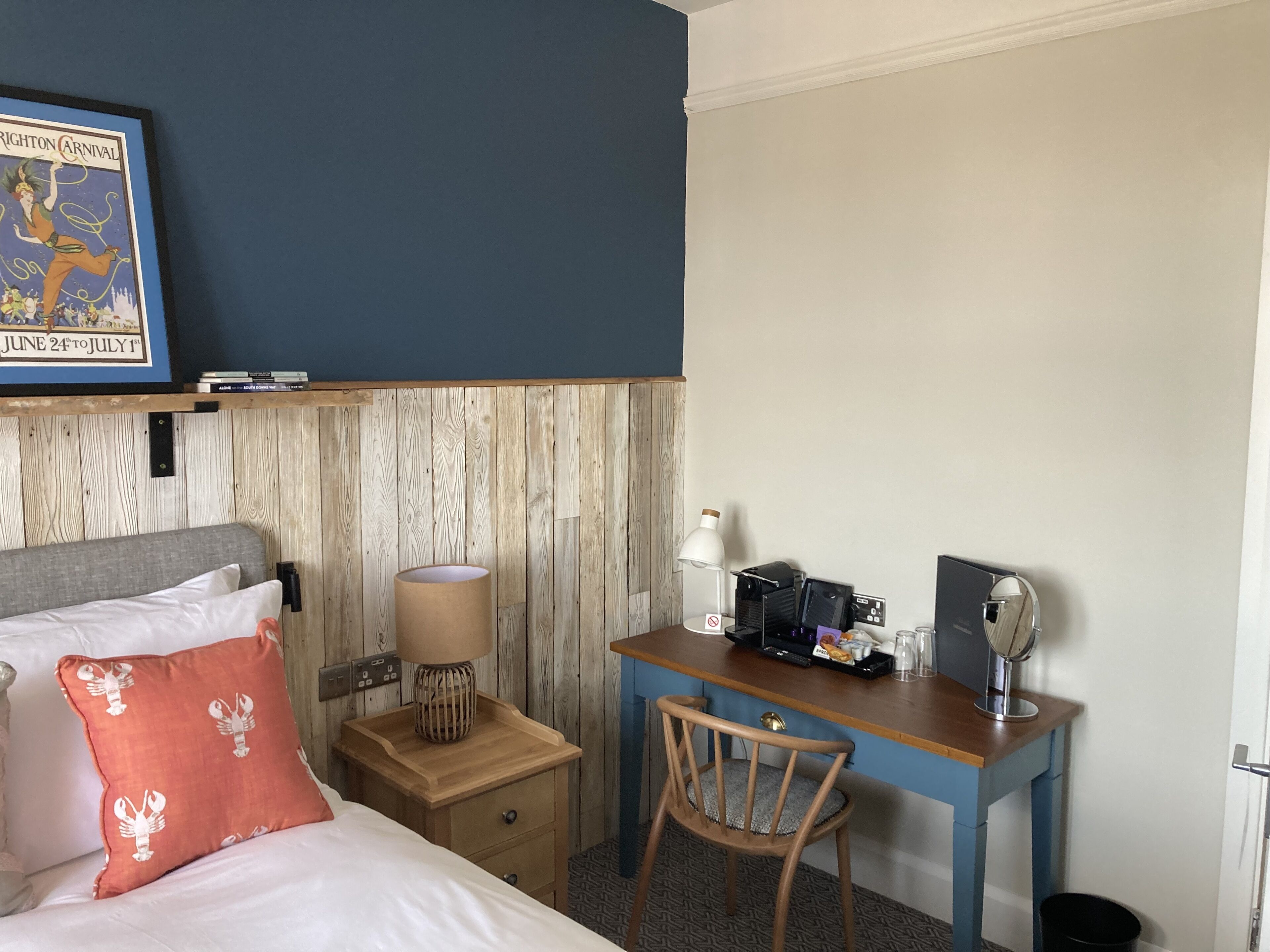 A hotel room with a bed, a desk with a computer, a lamp, and a small table.
