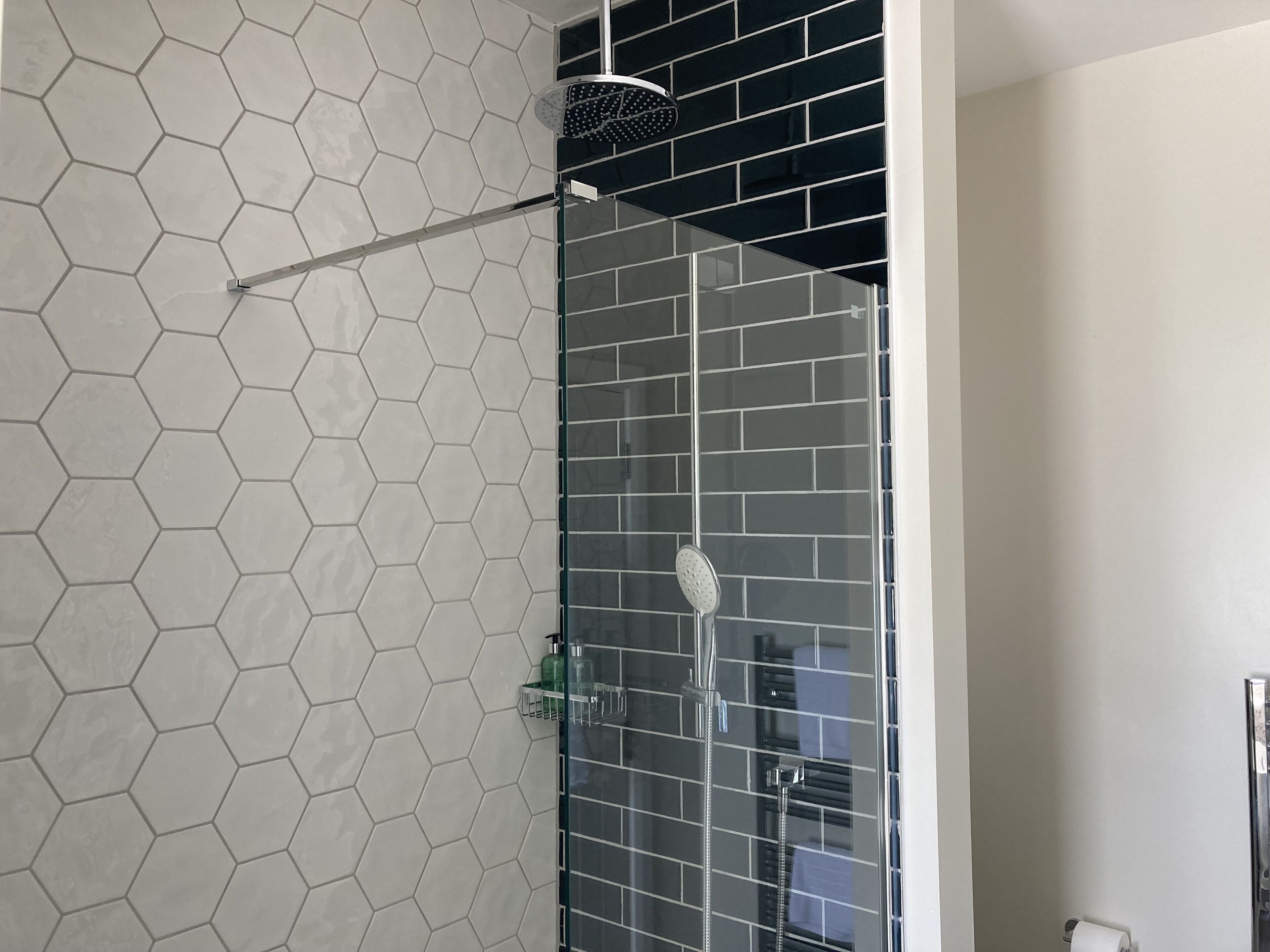 A shower with a glass door, a hexagonal tile wall, and a black tiled section.