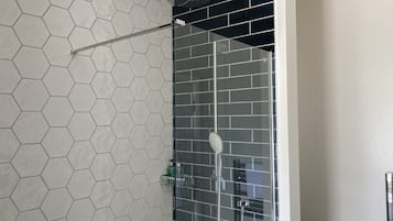 A shower with a glass door, a hexagonal tile wall, and a black tiled section.