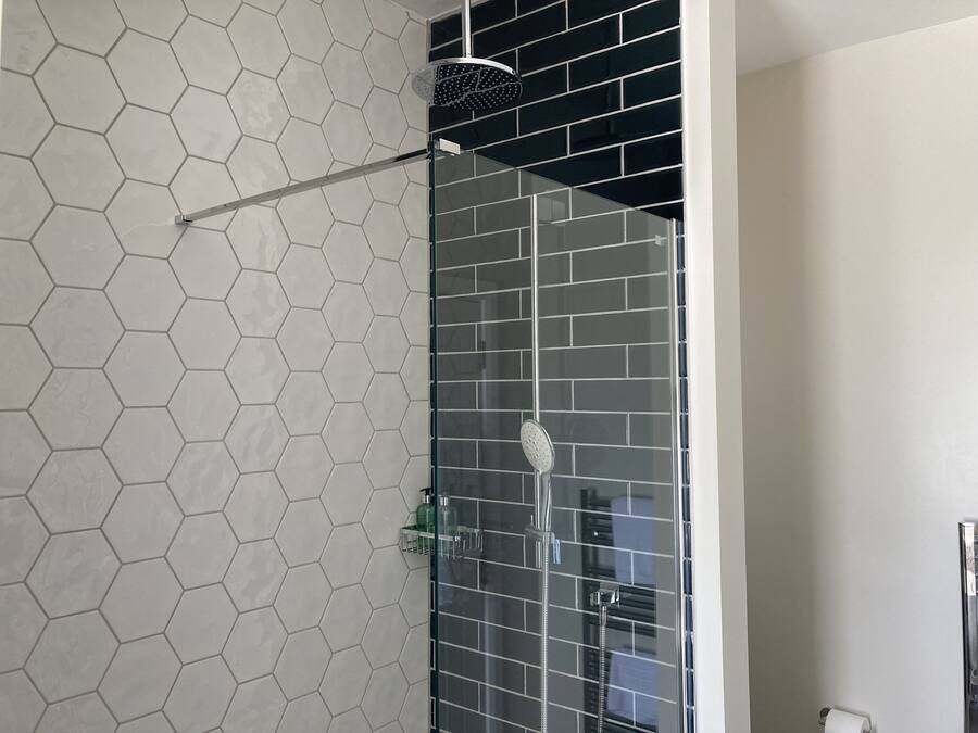 A shower with a glass door, a hexagonal tile wall, and a black tiled section.