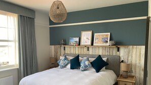 A bedroom with a large bed, a wooden headboard, a bedside table with a lamp, and a window with curtains. - Downs Hotel (Brighton)