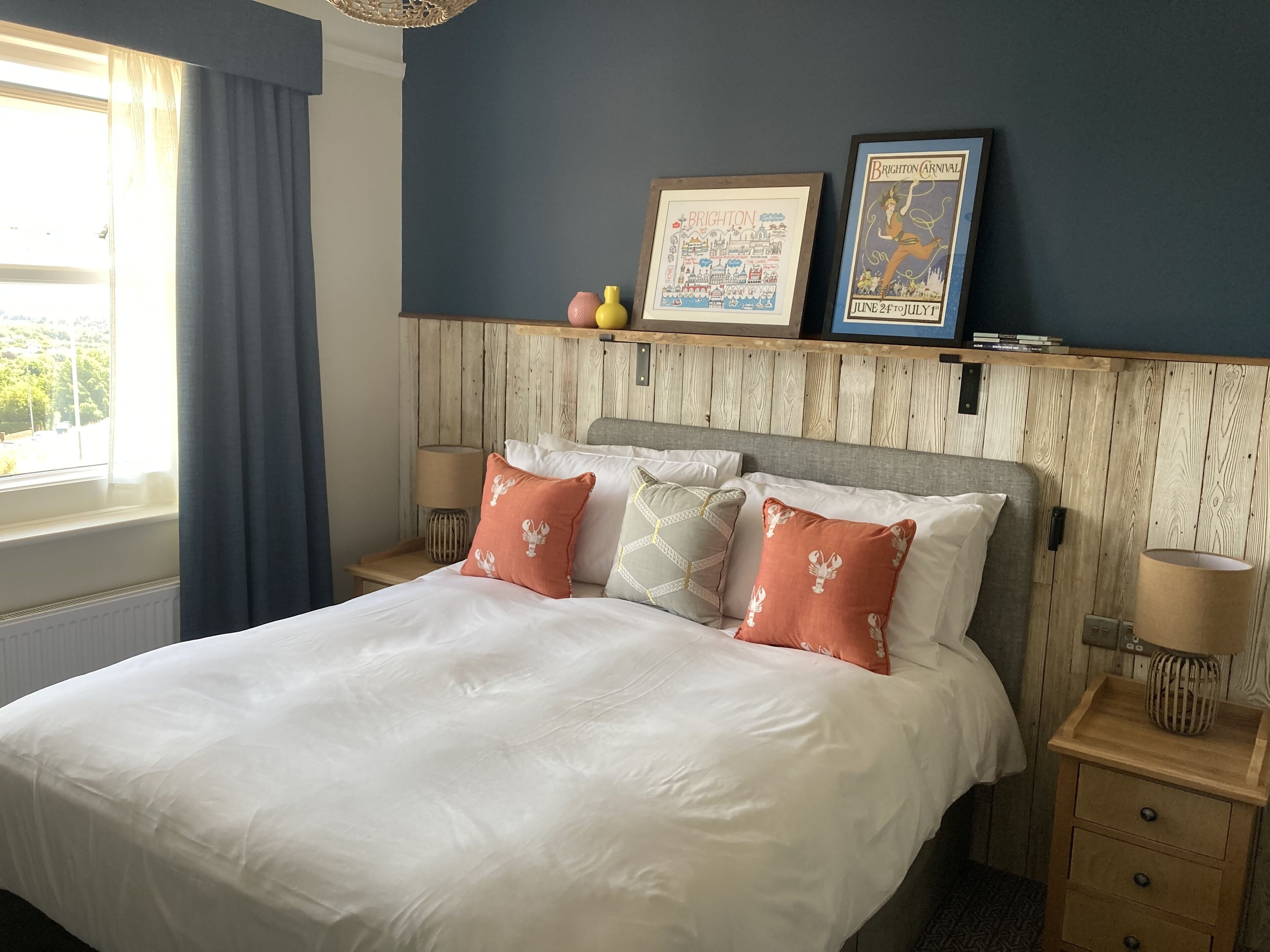 A hotel room with a large bed, wooden headboard, and two bedside tables. There are decorative pillows and a framed picture on the headboard.