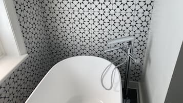 A bathroom with a white bathtub, a modern chrome faucet, and a geometric patterned wall.