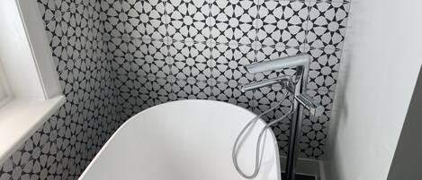 A bathroom with a white bathtub, a modern chrome faucet, and a geometric patterned wall.