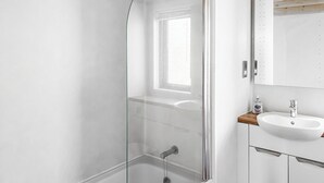 Une salle de bain moderne avec une douche à l’italienne en verre, un lavabo blanc et un plan de toilette en bois.