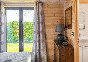 A wooden-paneled room with a bed, a dresser, a lamp, a mirror, and a bathroom with a sink and toilet.