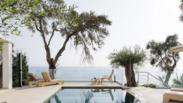 Une piscine à débordement avec des chaises longues et des arbres, offrant une vue sur la mer.