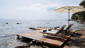 Une terrasse en bois avec des chaises longues et un grand parasol, le tout au bord de la mer.