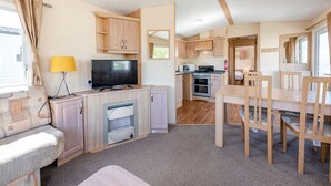 A compact RV kitchen with a TV, stove, microwave, and a dining area with chairs.