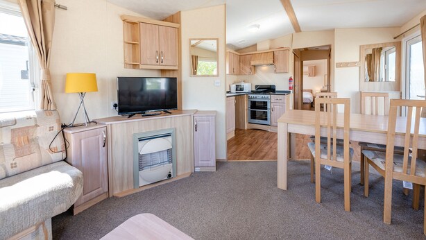 A compact RV kitchen with a TV, stove, microwave, and a dining area with chairs.