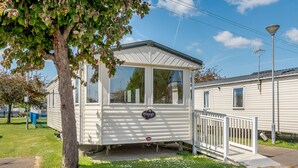 A mobile home with a small porch, a 'Presstige' sign, and a white fence.