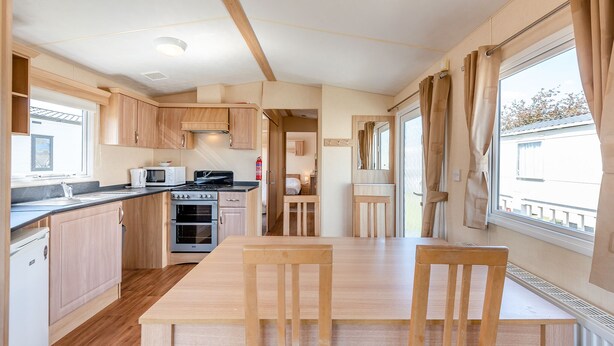 A compact kitchen with wooden cabinets, a microwave, stove, and a dining area with a table and chairs.