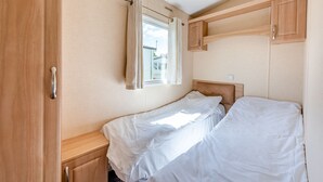 A small, single-bed room with a window, wooden cabinets, and a bedside table.