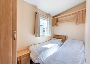 Ein kleines Zimmer mit einem Einzelbett, einem Fenster, Holzschränken und einem Nachttisch.