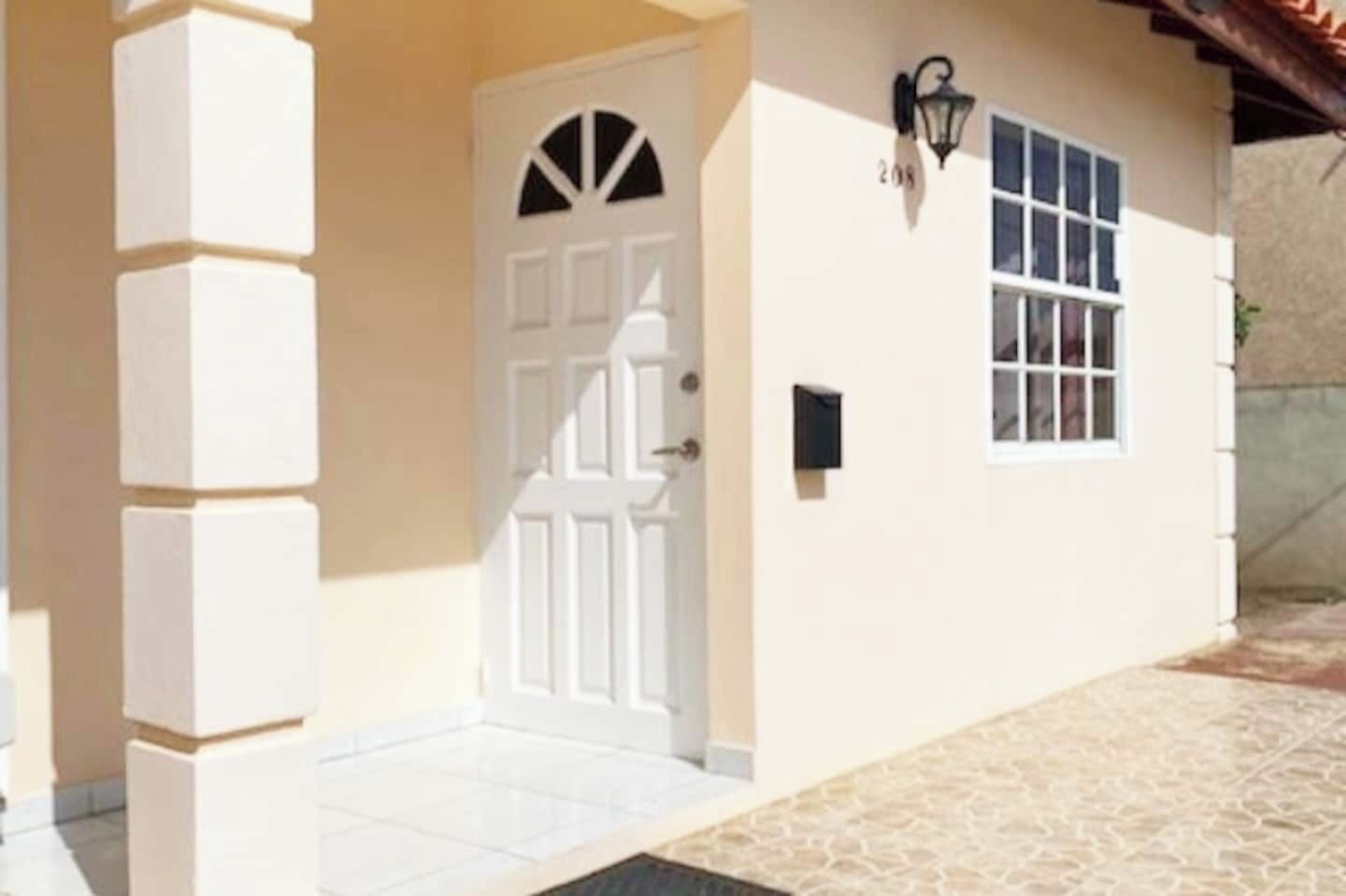 Um edifício com uma porta branca, janela com padrão quadriculado e uma pequena caixa de correio preta.