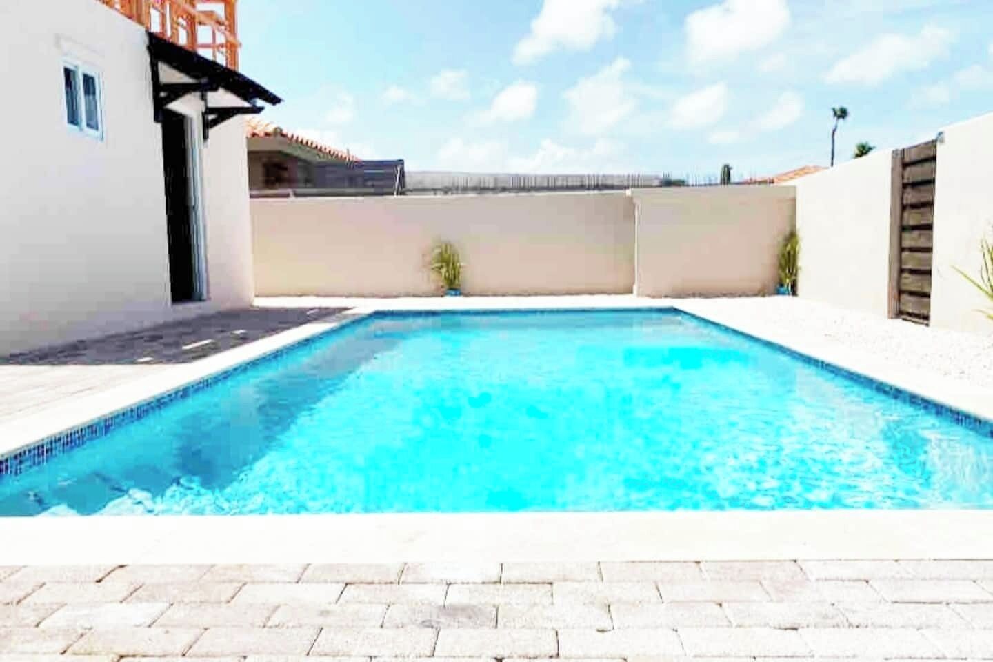 Une piscine rectangulaire dont les bords sont recouverts de carreaux, entourée d’une terrasse dallée.