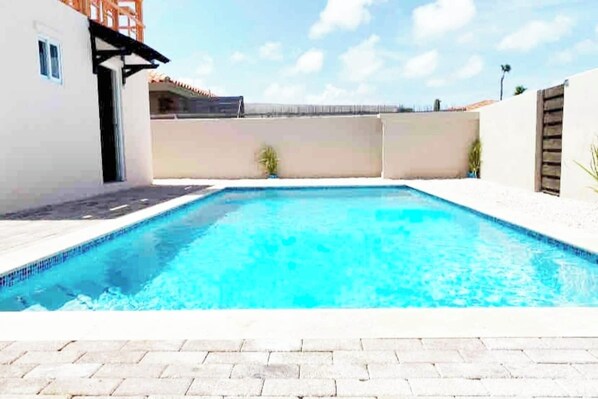 Una piscina rectangular con borde de azulejos, rodeada por un patio empedrado.
