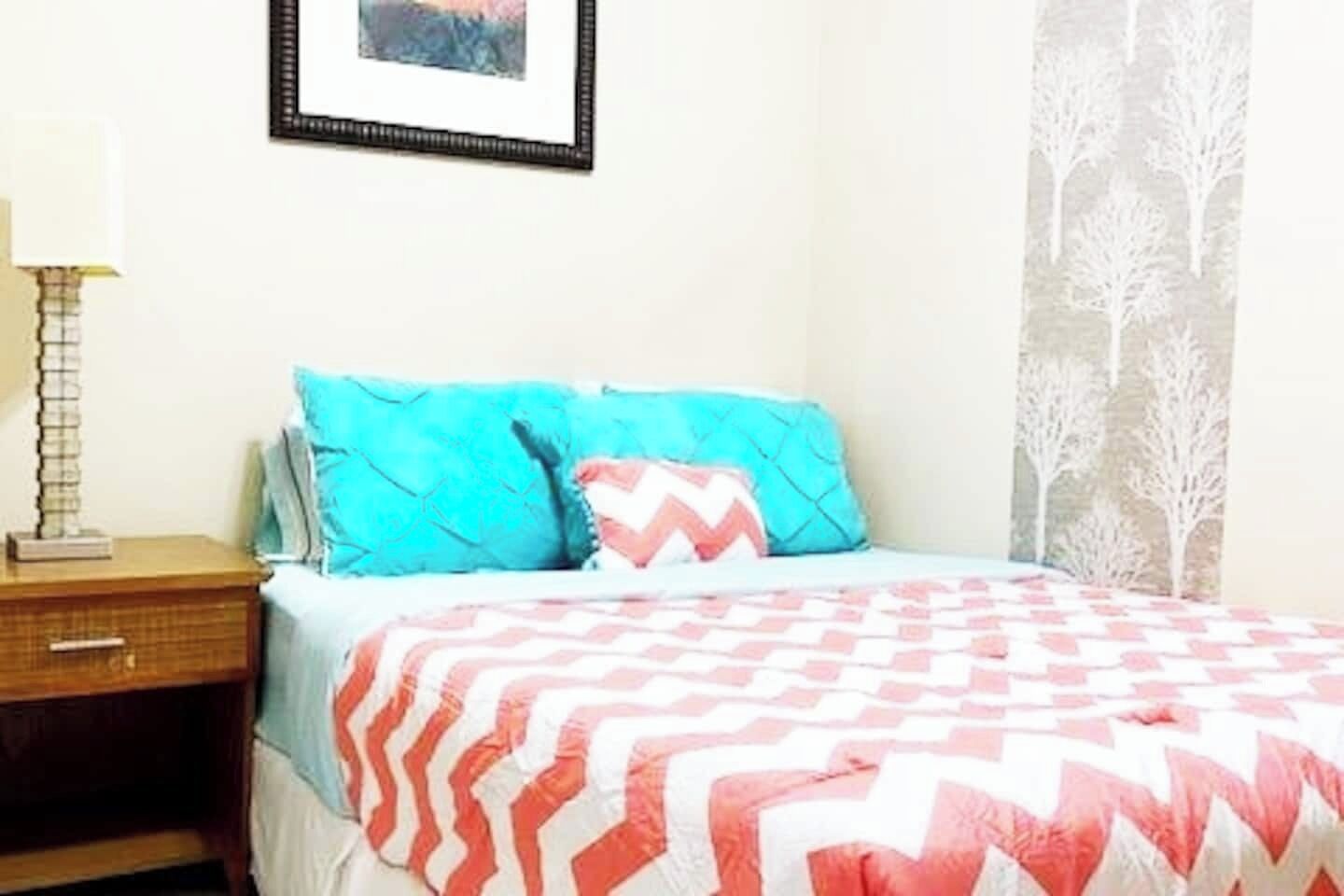 Una camera da letto con un letto, un comodino, una lampada e un quadro appeso al muro.