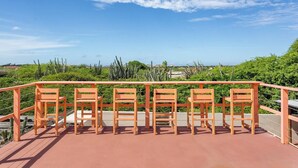 Eine Terrasse mit Geländer, Holzstühlen und Blick auf Kakteen und Grünpflanzen.